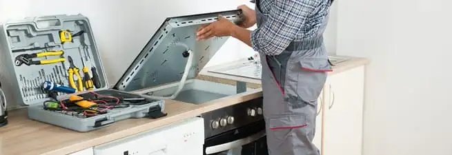 Cooktop repair technician lifting a built-in stovetop for service in Des Moines, IA