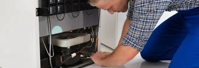 Refrigerator repair technician servicing the compressor and condenser area in Des Moines, IA