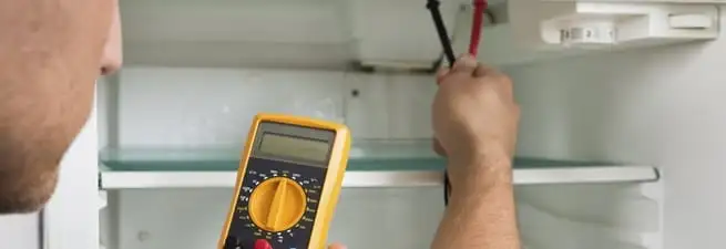 Refrigerator repair technician testing electrical components with a multimeter in Des Moines, IA