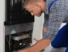 Refrigerator repair technician servicing the compressor and condenser area in Des Moines, IA